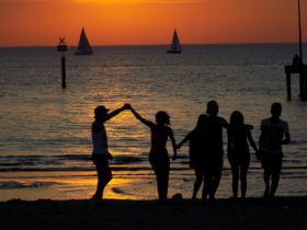 Picture shows a silhouette of people on a beach against the sunset.