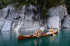 Picture shows a man and two children in a wooden canoe on clear blue water.
