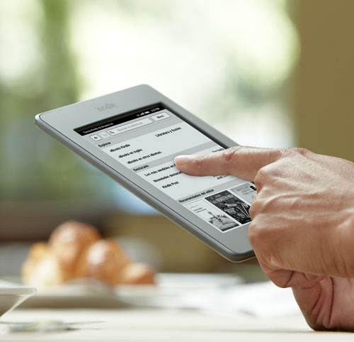 El e-reader Kindle Touch sostenido en la mano, con un dedo en la pantalla t�ctil